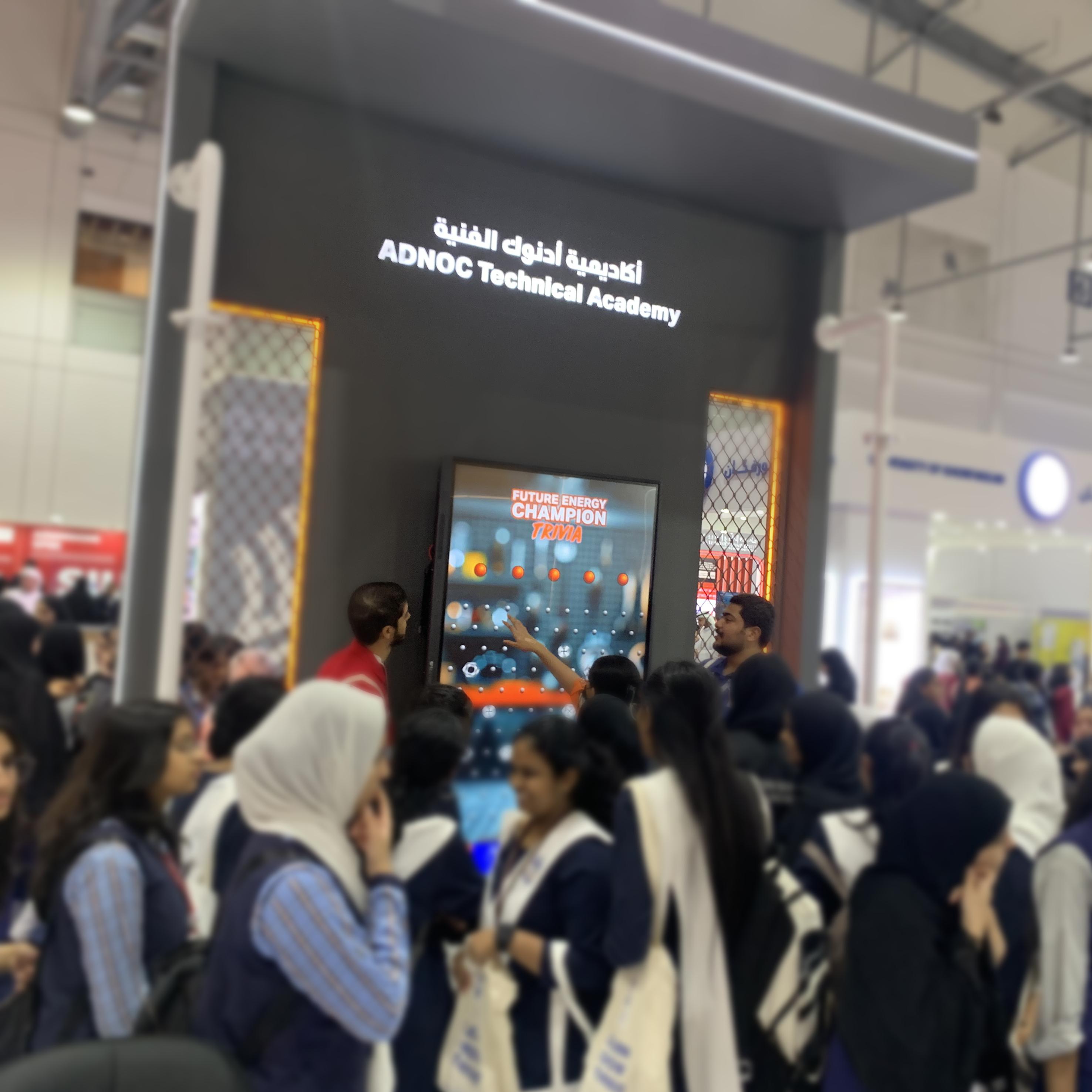 Students and guests play the Plinko Trivia Challenge at the ADNOC Technical Academy booth during a busy Dubai event